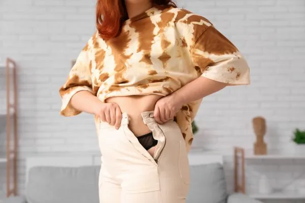 Image of woman trying to do her trousers up after pregnancy weight gain Ashtead