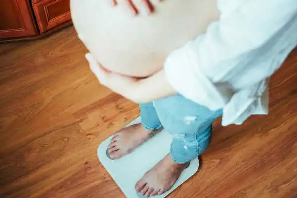 Image of woman weighing herself and experiencing weight gain through pregnancy Ashtead